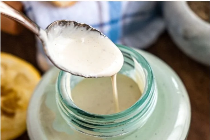 Healthy Caesar dressing in a glass bowl with fresh ingredients around it.